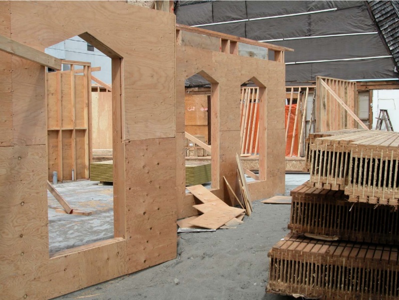 A photograph providing a detailed view of the wooden wall framing and at-grade concrete slab for the new multi-use facility, with the southern elevation of the 1964 Trinity Lutheran Church in the background.
