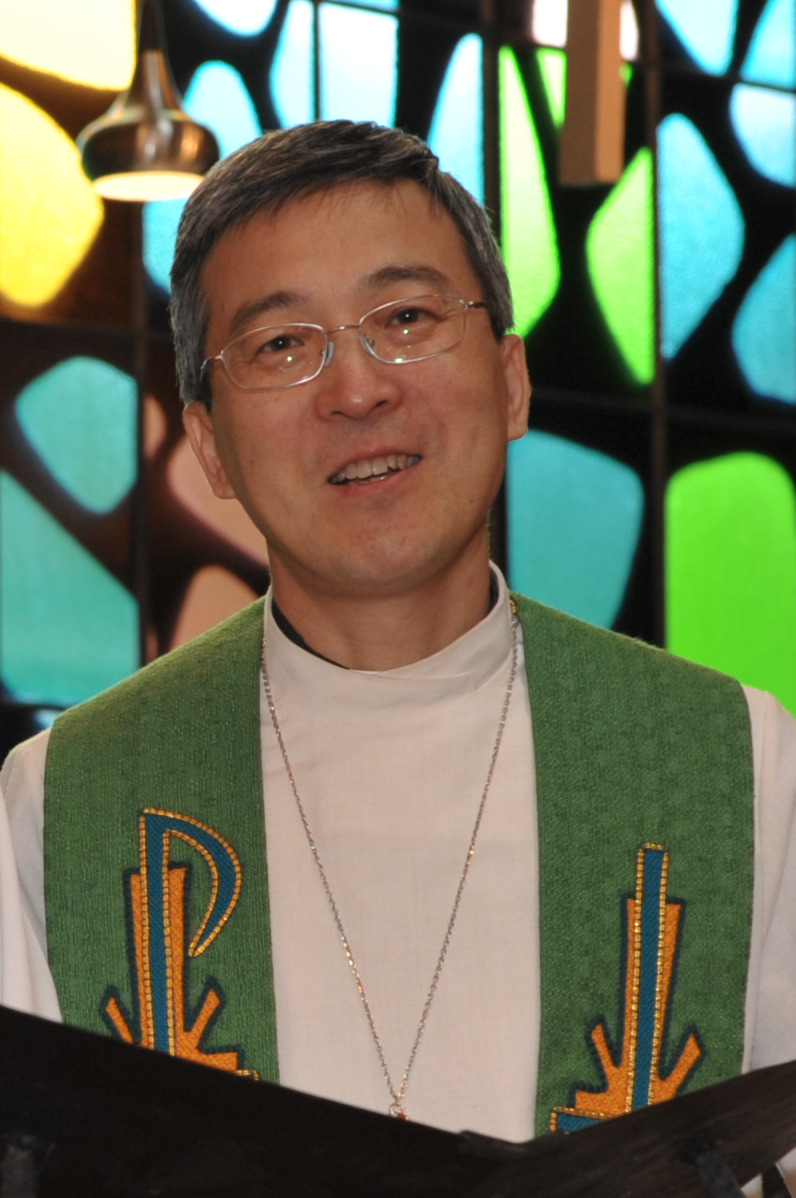 Portrait of Rev. Wayne Zhang, the Mandarin language Chinese ministries pastor at Trinity Lutheran Church in Richmond, standing at the pulpit wearing a green liturgical stole with embroidered Christian symbols.